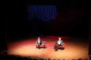 Kameraya ön planda, sahnede kadın ve erkek konuşmacılar, etkinlik ve toplantılar için ideal mekan.