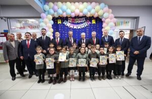 Neşeli çocuklar ve öğretmenler, balonlar ve kutlama süsleriyle dolu etkinlik alanında.